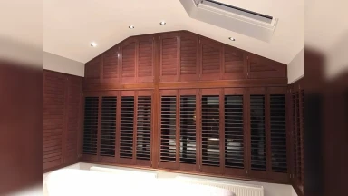 Mahogany coloured window shutters shaped to roof line