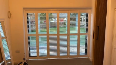 Semi open full height tracked window shutters looking out onto a garden lawn