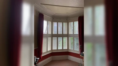 Tier on tier shutters in a bay window with red curtains